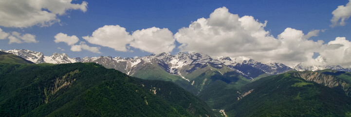 Lush green mountain slopes lead to snow-capped peaks under a clear sky, ideal for Earth Day and...