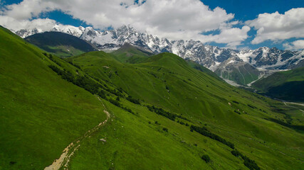 Breathtaking panoramic view of vibrant green meadows leading to snow-capped peaks under a blue sky, ideal for nature and travel themes, Earth Day promotions