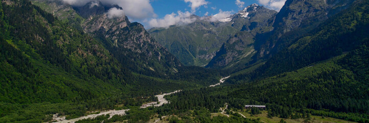 Breathtaking panoramic view of vibrant green meadows leading to snow-capped peaks under a blue sky, ideal for nature and travel themes, Earth Day promotions