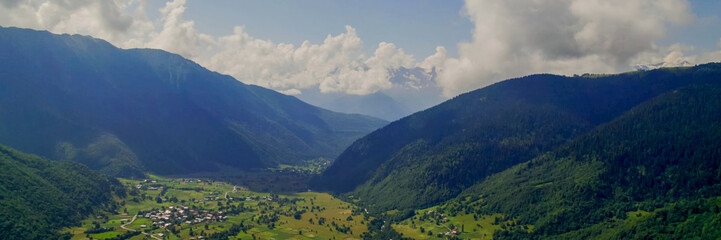Breathtaking panoramic view of vibrant green meadows leading to snow-capped peaks under a blue sky,...