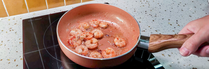 Close-up of a person's hand cooking shrimp in a frying pan, ideal for culinary blogs and seafood...