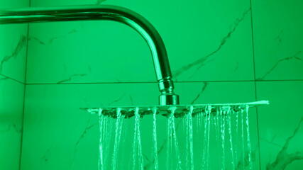 Modern showerhead with flowing water in a green-tinted bathroom, depicting concepts of hygiene,...
