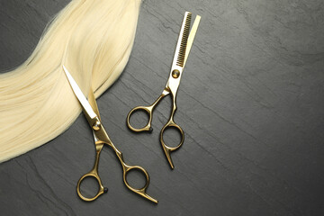 Professional hairdresser scissors with blonde hair strand on dark grey table, flat lay. Space for...