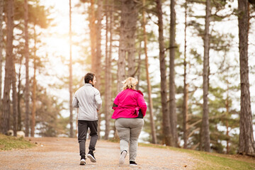 An overweight woman running in nature with friend. Exercising outdoors for people with obesity,...