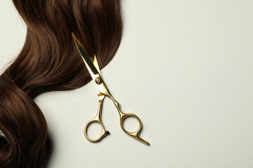Professional hairdresser scissors with brown hair strand on light grey background, top view. Space...