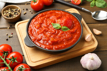 Homemade tomato sauce in bowl, spoon and ingredients on wooden table