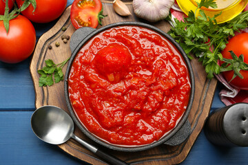 Homemade tomato sauce in bowl, spoon and ingredients on blue wooden table, flat lay