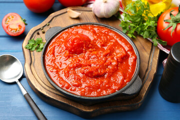 Homemade tomato sauce in bowl, spoon and ingredients on blue wooden table
