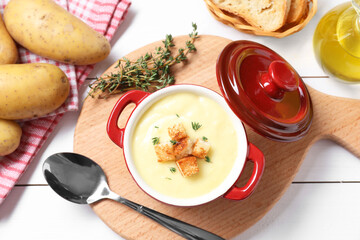 Tasty potato soup with croutons and rosemary in ceramic pot served on white wooden table, flat lay