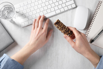 Woman holding tasty granola bar working with computer at light table, top view