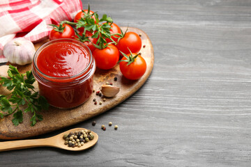 Tasty ketchup, fresh tomatoes, parsley and spices on grey wooden table, space for text