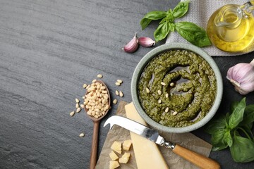Tasty pesto sauce, basil, pine nuts, cheese, garlic and oil on black table, flat lay. Space for text