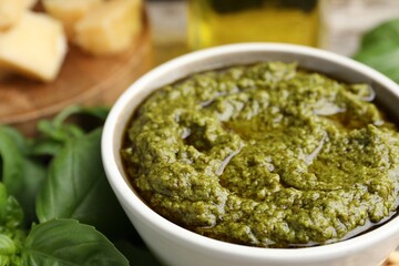 Tasty pesto sauce in bowl and basil on table, closeup