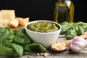 Tasty pesto sauce in bowl, pine nuts, garlic and basil on wooden table