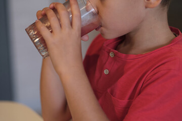 A young boy in a red shirt quenches his thirst with a glass of water, a subtle reminder of the...