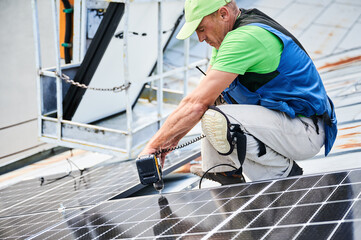 Worker building photovoltaic solar panel system on metal rooftop of house. Man technician...