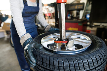 Female auto mechanic changing tieres in auto service, using machinery to removing tire. Beautiful...