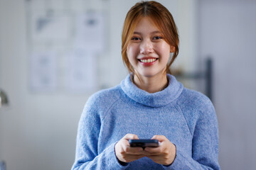 Happy young asian woman relax on comfortable couch at home texting messaging on smartphone, smiling...