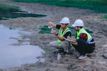 Portrait of asian male scientist and asian male biologist comparing test tubes with samples of polluted water, taken from mountain river and discussing results of analysis during research