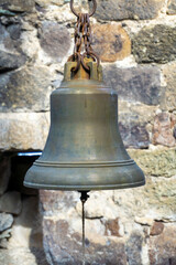 Obraz premium Brass old bell hanging on a rusty chain. Blurred stone wall on background