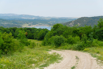 Earthen road leading to the Algeti reservoir. Green bushes and trees. Mountains, blue sky