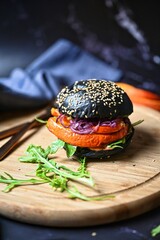 Vegan pumpkin burger with black bun with red caramelized onions and rocket, vertical shot