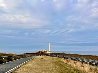 Asphalt road near a field with the St Mary's Lighthouse in the end of the road in UK