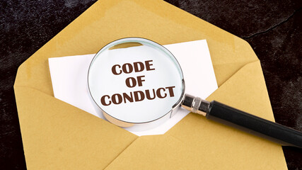 Business concept text. The words CODE OF CONDUCT on a white sheet of paper through a magnifying...