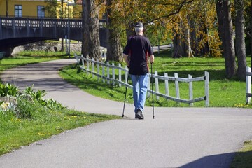 A senior with a Scandinavian stick walks along a city street. Active lifestyle in old age.
