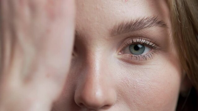 Attractive young woman covering one eye with her hand, looking at the camera.