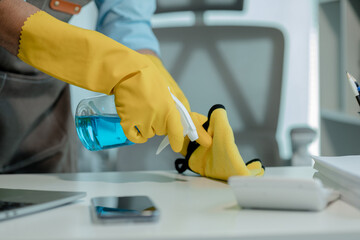 a cleaner is wiping everything in office with towel and sanitizer spray to remove all dust, wearing...