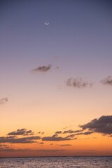 Beautiful view of an ocean during a sunset with dreamy clouds and a waxing crescent moon in the sky