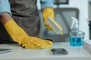 a cleaner is wiping everything in office with towel and sanitizer spray to remove all dust, wearing...