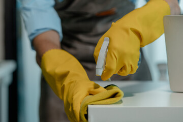 a cleaner is wiping everything in office with towel and sanitizer spray to remove all dust, wearing...