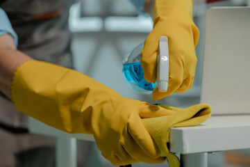 a cleaner is wiping everything in office with towel and sanitizer spray to remove all dust, wearing gloves to protect hands from chemical that use to cleanup all object for hygiene