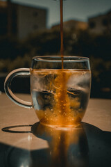 Vertical of coffee being poured into the glass cup filled with ice cubes