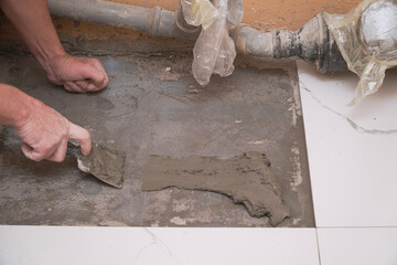 A construction worker applies cement for laying floor ceramic tiles with special spatula