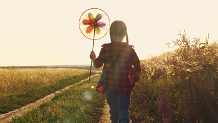 the pinwheel begins to play, child kid runs through park windmill hands, smile face, hand spinning sun, children dream, happy little girl child kid playing with a windmill at sunset, children running