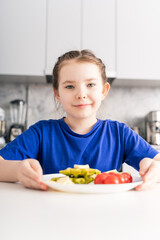 Portrait of a happy little girl having breakfast in the kitchen at home. Healthy breakfast of waffles with spinach, cheese and tomatoes. Selected focus.