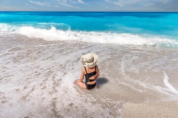 Obraz premium Woman in a big sun hat enjoying the foamy waves of a sea against a blue sky background