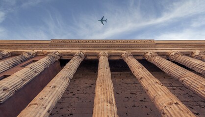 Low angle shot of the ancient columns and an aeroplane flying in the sky
