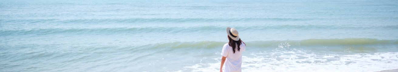 Rear view image of a woman with hat standing on the beach with blue sky background