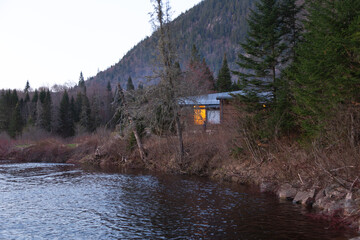 Wooden cabin with lighted window seen at dusk overlooking the river in the Jacques-Cartier National Park, Stoneham-et-Tewksbury, Québec, Canada