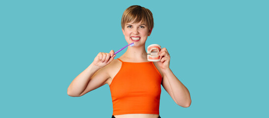 A smiling young woman with a jaw model and a toothbrush on an isolated blue background....