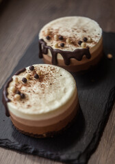 three-layer mousse dessert with chocolate and chocolate chips and crispy balls on a black stone board on a wooden table, close-up with blurred background. food photography, sweets.
