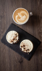 three-layer mousse dessert with chocolate and chocolate chips and crispy balls on a black stone board on a wooden table, close-up with cappuccino in a white cup top view. food photography, sweets.
