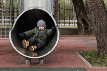 A little boy of 4 years old is walking around the playground. The child is having fun riding down the slide. Childhood and child development.