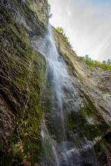 Waterfall hidden inside the forest, beauties of Slovenia to be discovered. Near Nova Gorica, Tolmin village. Water spray and vivid rainbow forms from the waterfall that falls sheer onto the rock.