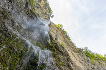 Waterfall hidden inside the forest, beauties of Slovenia to be discovered. Near Nova Gorica, Tolmin village. Water spray and vivid rainbow forms from the waterfall that falls sheer onto the rock.