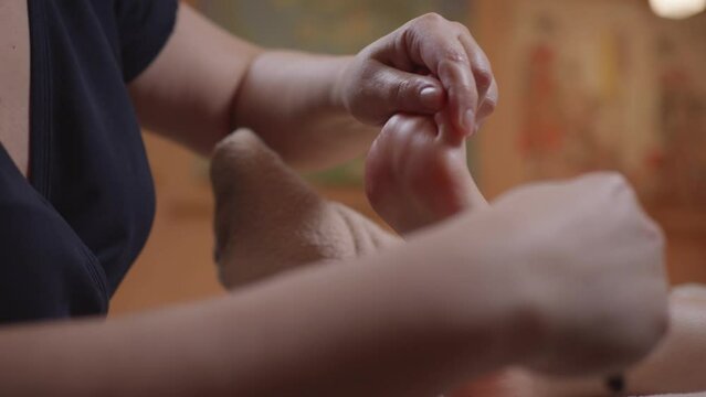 Thai feet massage using a bamboo massage stick in spa to a young girl close-up